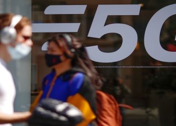 People, wearing protective face masks, walk past a 5G data network sign at a mobile phone store in Paris, France, April 22, 2021. REUTERS/Gonzalo Fuentes